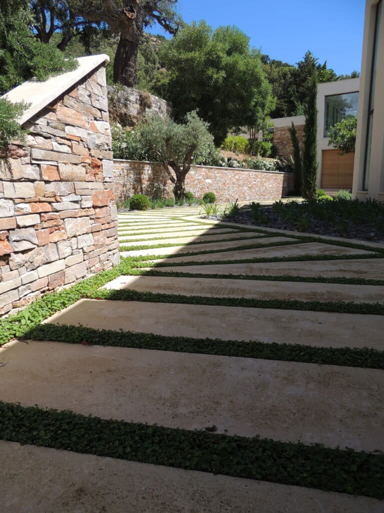 Aménagement de jardin moderne avec allée en dalles de pierre Allée design en dalles de béton et gazon avec mur en pierre naturelle devant une villa contemporaine.