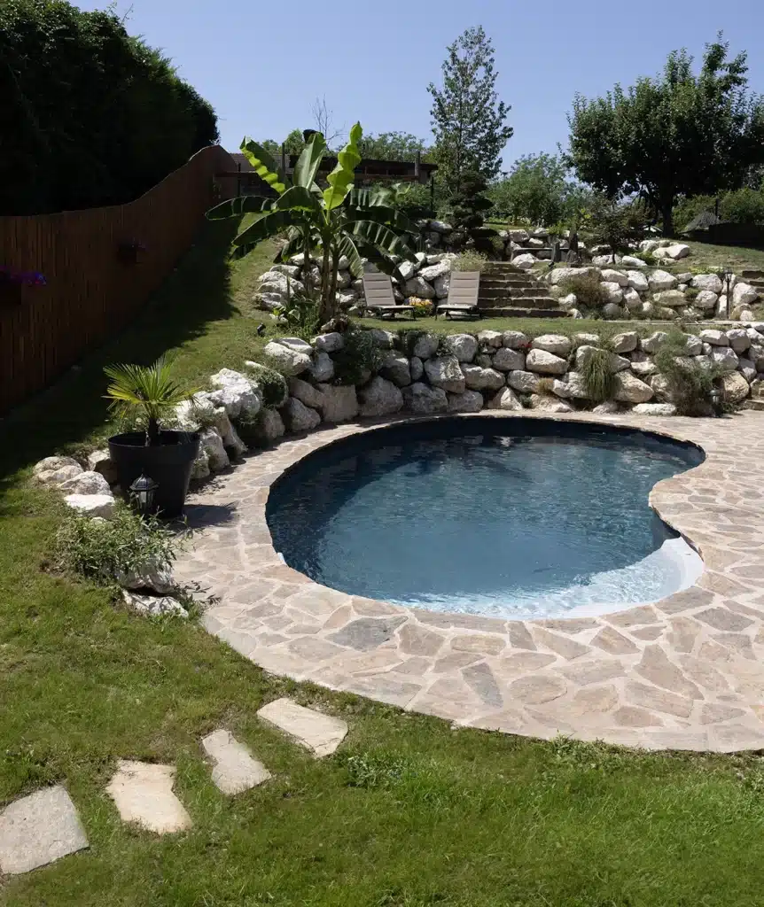 Aménagement piscine avec terrasse pierre et rocaille Piscine haricot entourée de pierres naturelles, murets de rocailles et bananier dans un jardin paysager.
