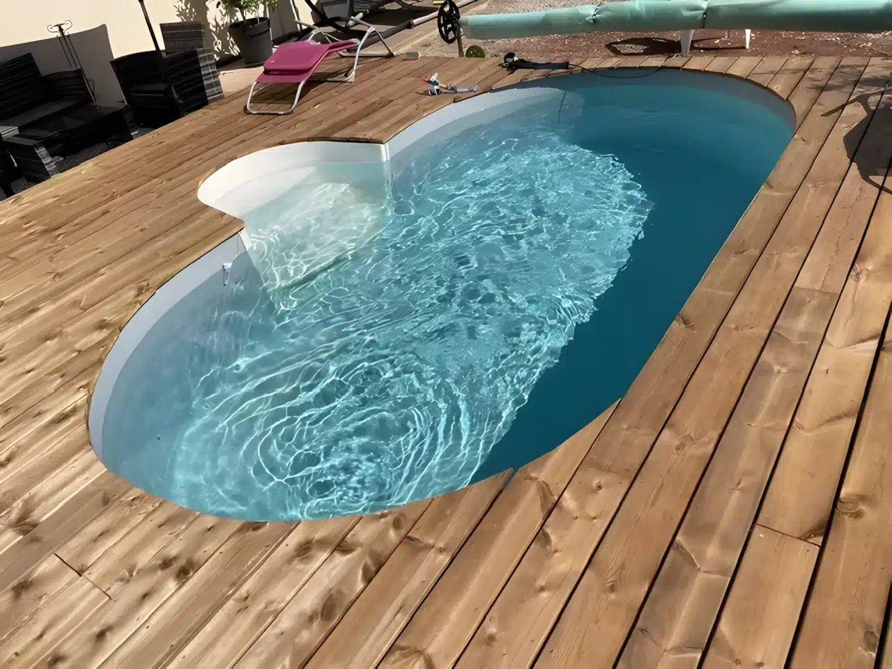Petite piscine ovale encastrée dans une terrasse en bois avec eau bleue scintillante et transat rose.